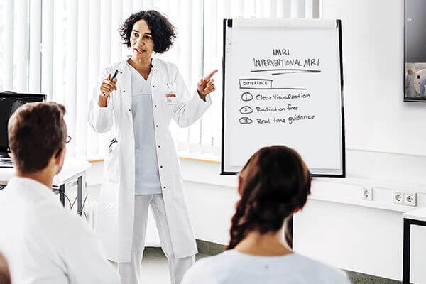 A presenter points at a display board describing the benefits of iMRI as she explains to two listeners.