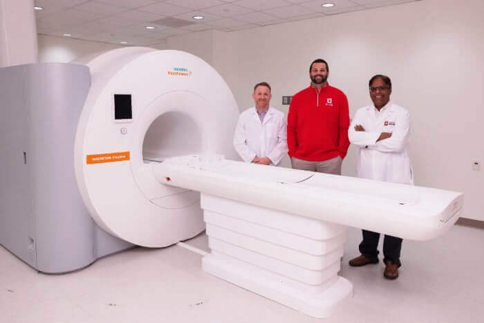 Three men posing next to a Siemens MRI machine.