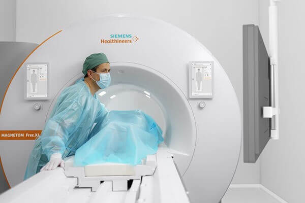 A doctor tending to a patient in an MRI machine while observing a suspended monitor.