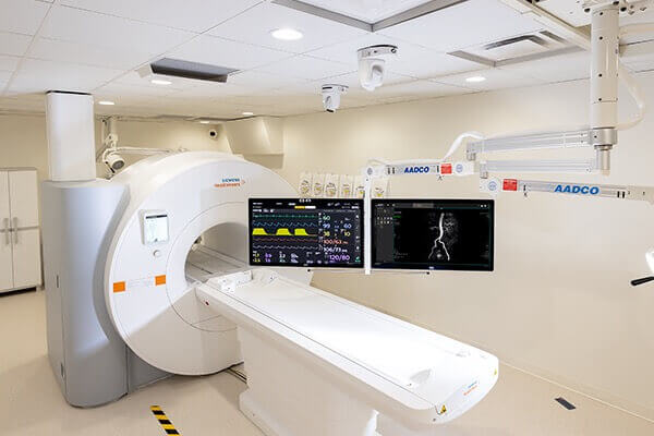 An MRI suite, with an MRI machine and suspended monitors displaying results.