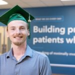 Cook Medical employee Duncan Gage stands in front of inspirational signage wearing his HSE graduation cap