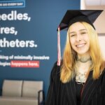 Cook Medical employee Juliana Swoape poses in her HSE cap and gown in front of inspirational signage at headquarters