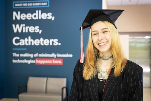 Cook Medical employee Juliana Swoape poses in her HSE cap and gown in front of inspirational signage at headquarters